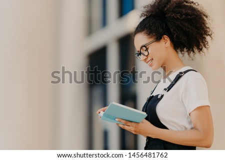 [[stock_photo]]: Profile Shot Of Curly Girl Focused In Organizer Learns Her Plans For Next Week Has Positive Expres