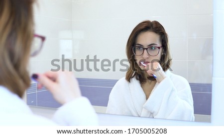 [[stock_photo]]: Pretty Female Brushing Her Teeth In Front Of Mirror In The Morning