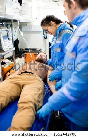 Foto stock: Young Female Paramedic Giving First Aid To Sick Shirtless Man On Stretcher