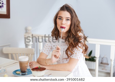 Stok fotoğraf: Beautiful Woman With Spoon In Her Mouth Sitting At A Table With Latte Macchiato Coffee