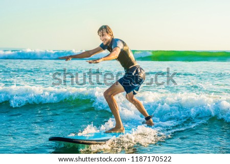 Stockfoto: Young Man Beginner Surfer Learns To Surf On A Sea Foam On The Bali Island