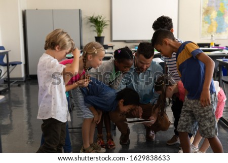 Foto stock: Front View Female Teacher Teaching Schoolboy On Digital Tablet At Table In Classroom Of Elementary S