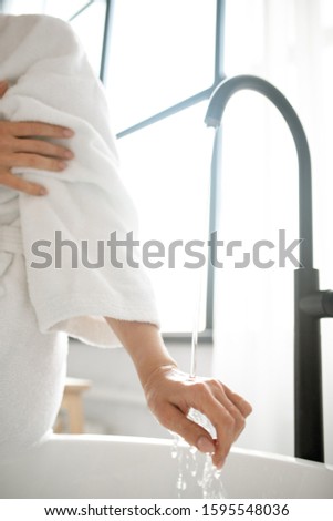 Foto d'archivio: Hand Of Young Woman Checking Temperature Of Water Flowing From Tap Into Bathtub