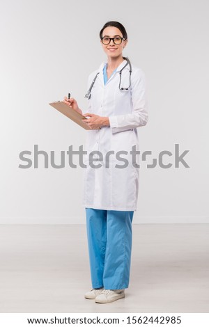商業照片: Young Confident Clinician In Whitecoat Filling In Medical Document In Isolation