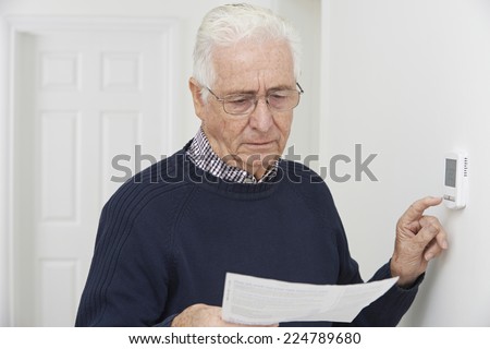 Foto stock: Worried Senior Man With Bill Turning Down Central Heating Thermo