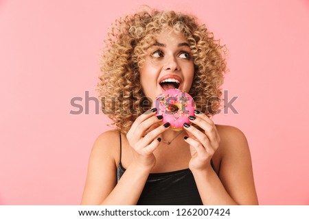 Foto stock: Of Joyful Curly Woman 20s Wearing Dress Eating Donut While