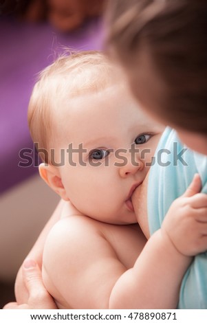 Stockfoto: Mother Is Breastfeeding A Baby Sitting On A Chair Close To The Window
