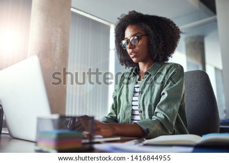 Сток-фото: Serious Curly Young Businesswoman Sitting By Workplace In Front Of Laptop