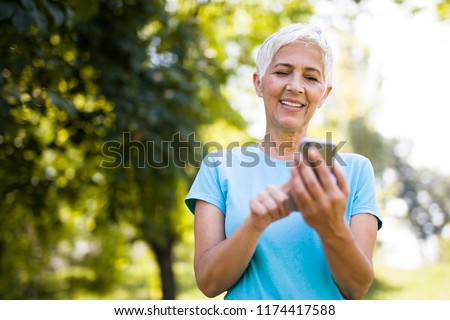 Stok fotoğraf: Portrait Of Sporty Senior Woman Using Mobile Phone In The Park