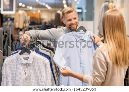 Foto stock: Young Couple Choosing Shirt For Man While Standing By Rack With New Collection