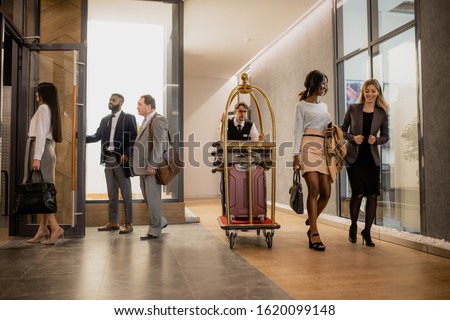 Stockfoto: Busy Porter Pushing Cart With Baggage While Moving Among Business People