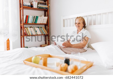Zdjęcia stock: Elderly Woman Having Breakfast In Bed Whilst Using Her Tablet