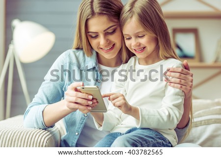 ストックフォト: Happy Mother Embracing Her Daughter With Smartphone While Both Watching Video