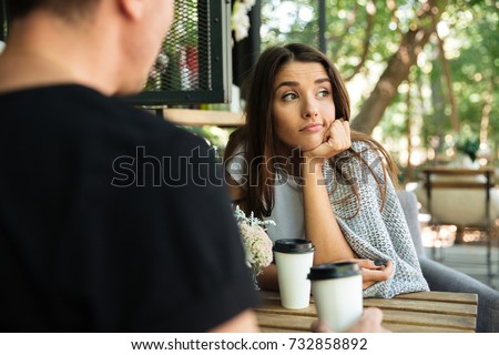 Foto d'archivio: Young Bored Girl Sitting And Drinking Coffee With Her Boyfriend