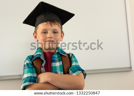 Сток-фото: Low Angle View Of A Happy Caucasian Boy In Graduation Cap Standing In A Classroom At Elementary Scho