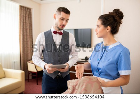 Foto stock: Young Pretty Room Maid Looking At Porter While Showing Him Stain On Blanket