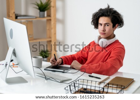 Foto d'archivio: Young Male Freelancer With Headphones Looking At You While Retouching Photos