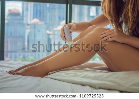 Сток-фото: Young Woman Sitin On Bed At Home And Doing Epilation With Epilator On Legs And Is In Pain On The Ba