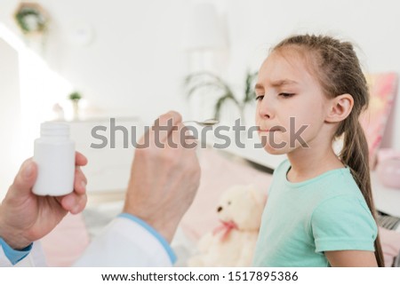 Stockfoto: Cute Little Girl Looking Reluctantly At Medicine In Spoon Held By Her Doctor