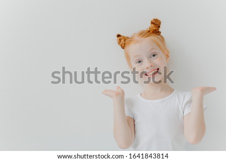 Foto stock: Playful Red Haired Girl Raises Palms Has Double Buns Looks Happily At Camera Wears Casual White T