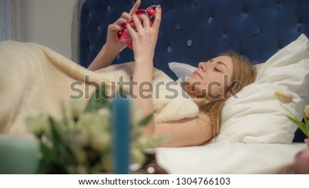 Foto d'archivio: Red Haired Woman Lying In Bed Turning Off Alarm Clock In Her Bedroom