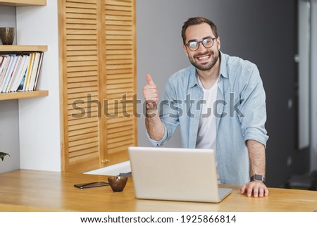 Foto stock: A Young Man In Glasses Stands Near A Computer Desk And Is Talking On The Phone Before Him Lies A Ma