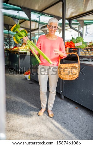Stockfoto: Senior Woman Holds Basket With Flowers And Buys Lettuce On Mark