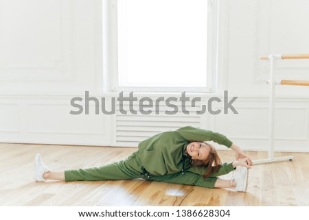 [[stock_photo]]: Flexible Slim Woman With Ginger Hair Does Leg Split Has Stretching Exercises Poses In Home Interi