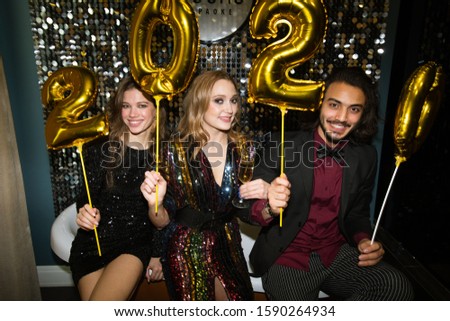 Foto stock: Three Young Friends In Glamorous Attire Holding Golden Inflatable Numbers