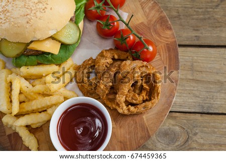 Foto d'archivio: Hamburger Onion Ring Tomato Sauce Cherry Tomato And French Fries On Chopping Board