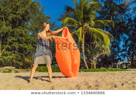 Stock fotó: Summer Lifestyle Portrait Of Woman Inflates An Inflatable Orange Sofa On The Beach Of Tropical Islan