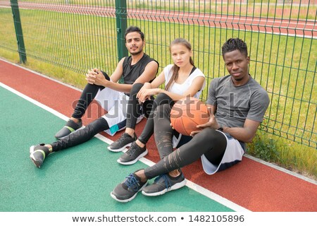 Сток-фото: Three Young Athletes In Sportswear Sitting On Outdoor Basketball Court By Net