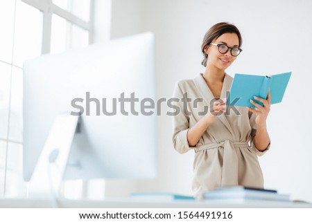 Stock fotó: Cheerful Female Director Holds Personal Organizer Looks Through Plans For Day Wears Beige Formal C
