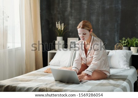 Stock fotó: Busy Young Female In Pajamas Having Hydrating Textile Mask On Face While Typing