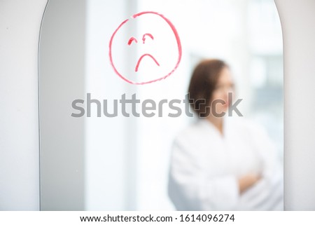 Foto stock: Upset Face Drawn By Red Or Crimson Lipstick On Mirror On Background Of Sad Girl