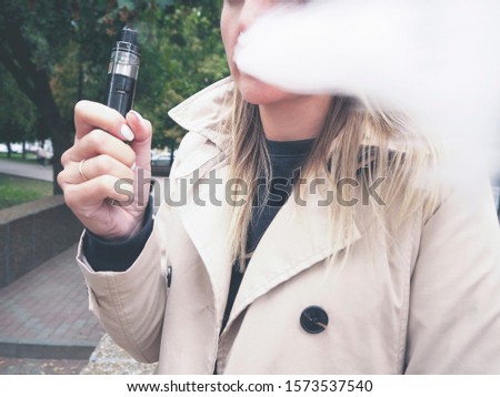 Stok fotoğraf: Blond Girl In Beige Trench Coat Vaping Fruit E Liquid With Very