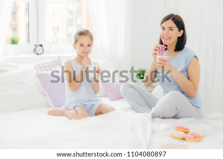 Zdjęcia stock: Cheerful Mother And Daughter Dressed In Pyjamas Have Breakfast In Morning Drink Milk Shake With Do