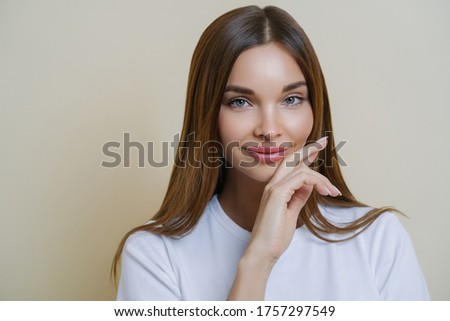 Сток-фото: Close Up Shot Of Charming Dark Haired Woman Keeps Hand On Cheek Dressed In Casual White T Shirt Ha