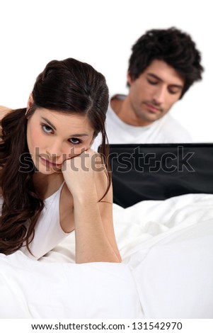 Сток-фото: Girl In Bed Looking Bored And Companion In Background With Laptop