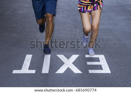 [[stock_photo]]: Young Man And Woman Jogging Together On Street With Exit Sign