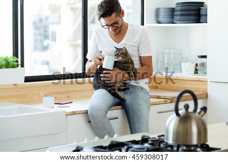 Stok fotoğraf: Portrait Of Handsome Young Man Playing With Cat And Drinks Coffee