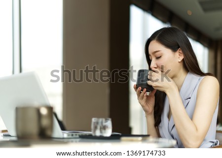 Zdjęcia stock: A Young Girl Is Sitting At A Table In The Office Holding A Red Cup In Her Hand And Working With Doc