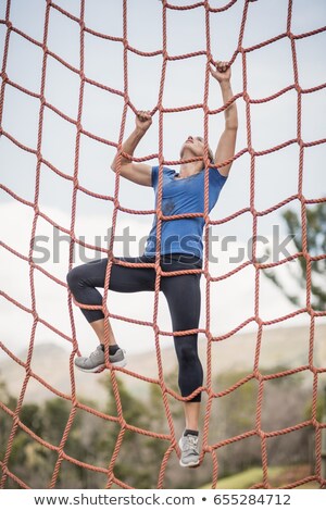 Foto d'archivio: Fit Woman Climbing A Net During Obstacle Course Training