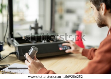 Foto stock: Young Engineer Holding Detail Of 3d Printer While Checking The Machine