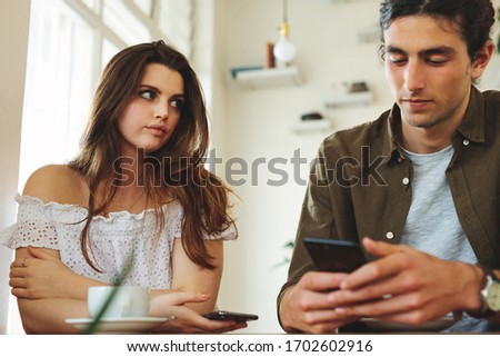 Foto stock: Displeased Young Man Looking At Mobile Phone Of His Woman Chatting In Jeans Denim Jackets Isolated O