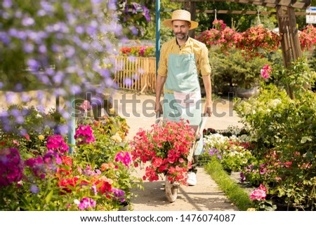 Mature Farmer In Hat And Apron Moving Along Flowerbeds In His Garden Foto stock © Pressmaster