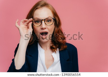 Stok fotoğraf: Headshot Of Surprised Red Haired Woman Keeps Hand On Frame Of Glasses Jaw Dropped Can Not Believe