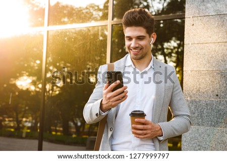 Foto stock: Smiling Businessman Walking And Using Mobile Phone Near Business Center