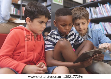 Zdjęcia stock: Side View Of Schoolboys Using A Digital Tablet While They Are Sitting On Cushions In A Library At Sc