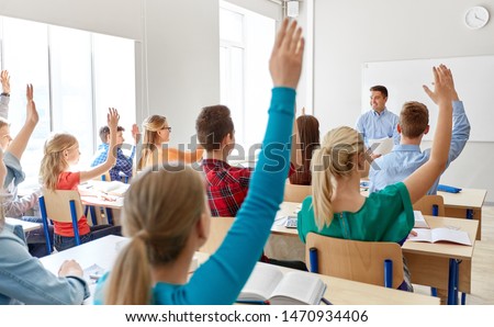 Stockfoto: Rear View Of School Kids Raising Hand To Answer At A Question Asking By Their Teacher Standing In Fr